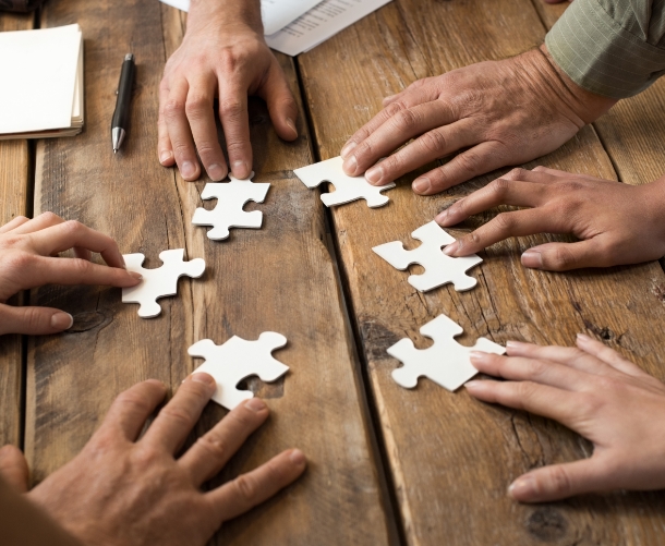 Hands of diverse people assemble a jigsaw puzzle signifying that teamwork is essential for finding solutions.