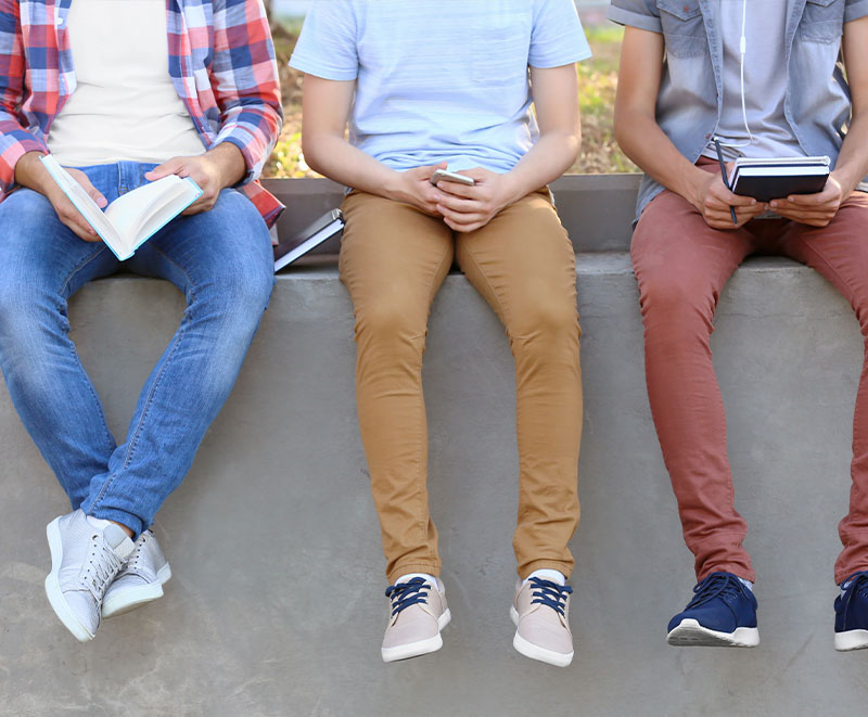 Young adults sitting on a cement wall outdoors talking and collaborating.