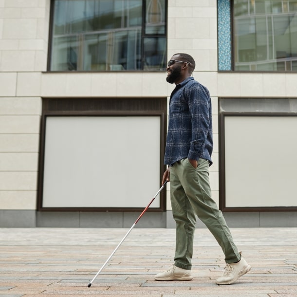 A man who is blind walks down the street using a white cane.